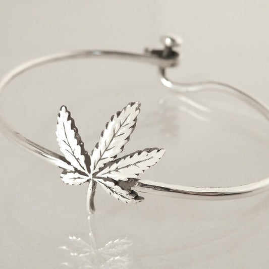 Silver bracelet with a cannabis leaf charm on a light gray background