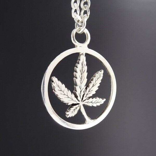 Silver pendant with a cannabis leaf design on a dark background