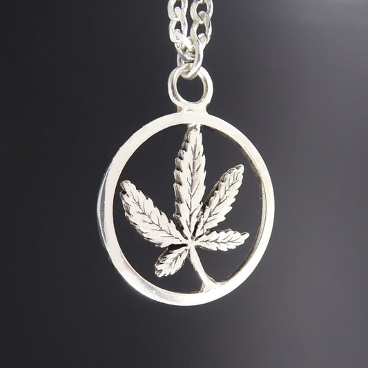 Silver pendant with a cannabis leaf design on a dark background